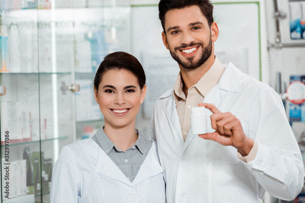 Pharmacists with jar of pills smiling at camera in drugstore Pharmacists with jar of pills smiling at camera in drugstore