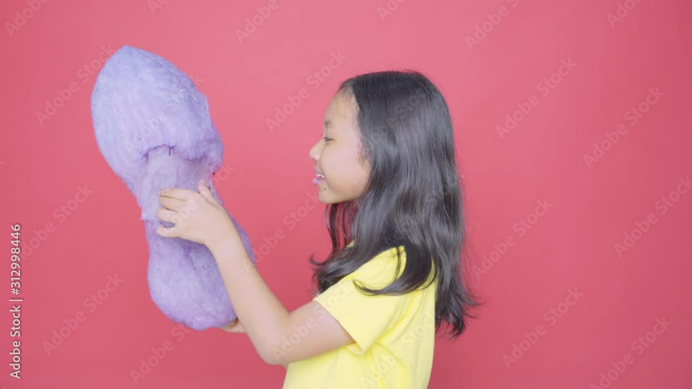 Adorable little girl eating a big cotton candy while standing in the studio. Shot in 4k resolution Adorable little girl eating a big cotton candy while standing in the studio. Shot in 4k resolution