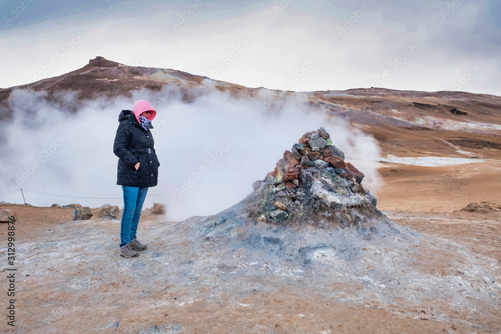 Woman traveler travels to Hverir in Iceland, looking at steam