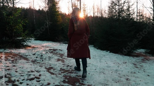 young blonde in a coat walks through a snowy forest photo