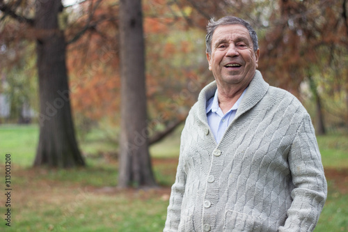 Portrait of happy senior man smiling, in the public park, outdoors.. Old man relaxing outdoors and looking at camera. Portrait of elderly man enjoying retirement