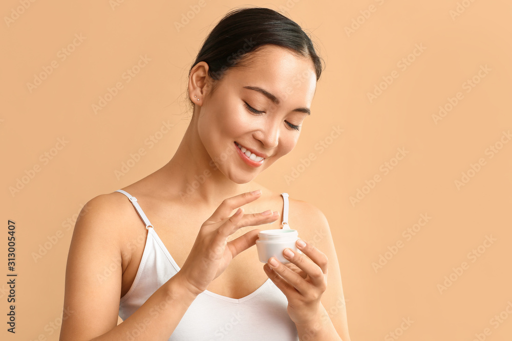 Beautiful Asian woman with jar of cream on color background Beautiful Asian woman with jar of cream on color background