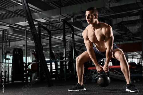 Sporty muscular man training with kettlebell in gym