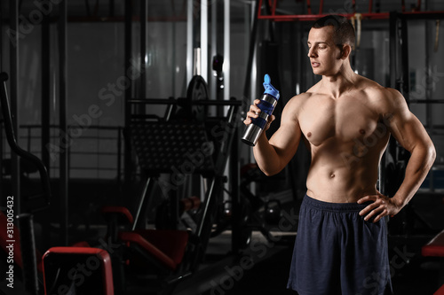 Sporty muscular man drinking water in gym