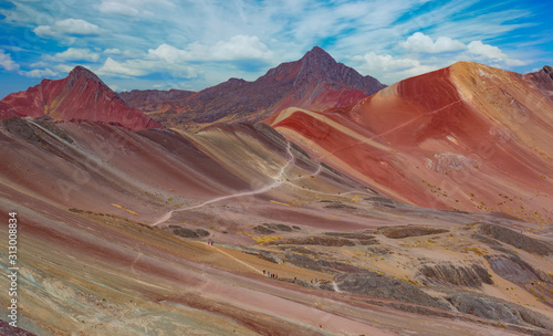 Landscape of hiking scene at Rainbow Mountain at Vinicunca Valley. Apu Ausangate is behind. All rocks, mountains and sand is invaded by red colors. Cusco Region, Peru