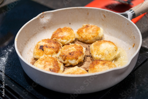Fishcakes frying in butter on a white skillet. The fishcakes are round and golden brown. 