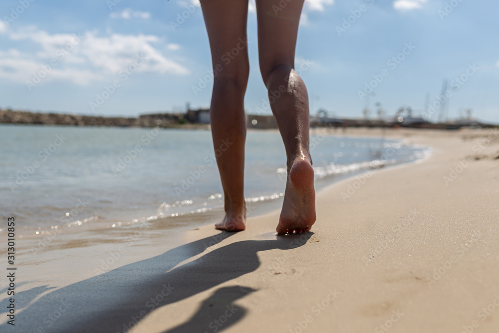 Beautiful tanned legs of a girl walking in the water. The girl runs through the sea water on the edge of the beach. Beautiful tanned legs of a girl walking in the water. The girl runs through the sea water on the edge of the beach.