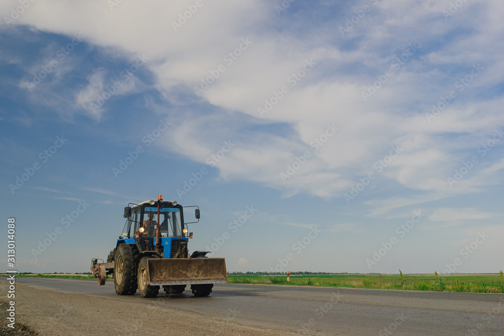 tractor rides on the road in summer against the blue sky in summer. focus on the tractor