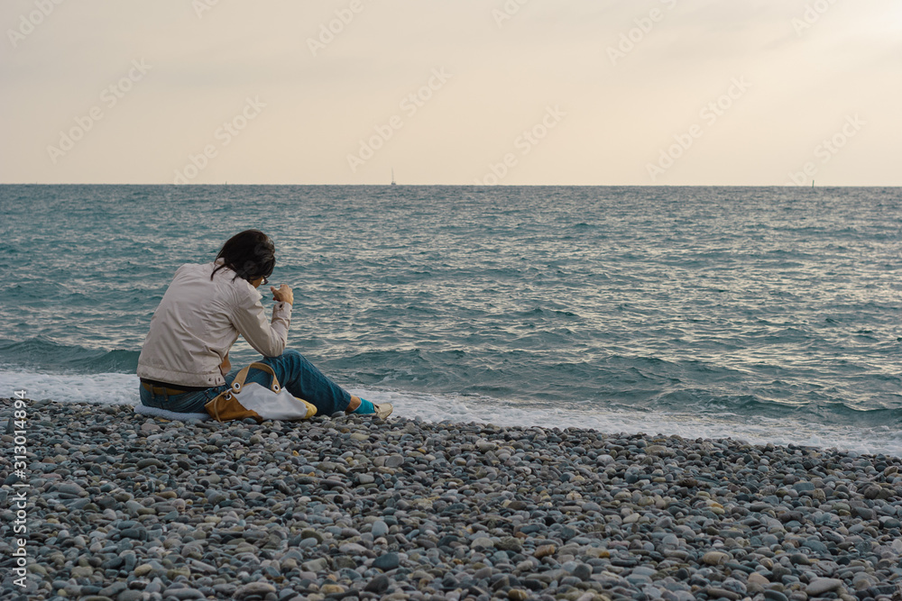 a woman sits on a shingle by the sea and looks into the distance. focus on the woman