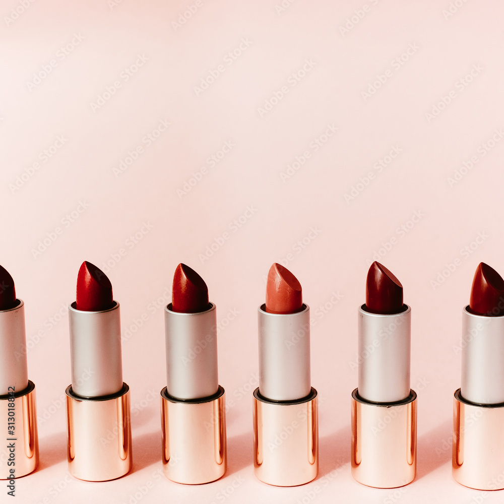 Obraz premium Multi-colored lipsticks stand in a row on a pink background. The concept of different, collections and beauty. Red, pink and burgundy lipsticks