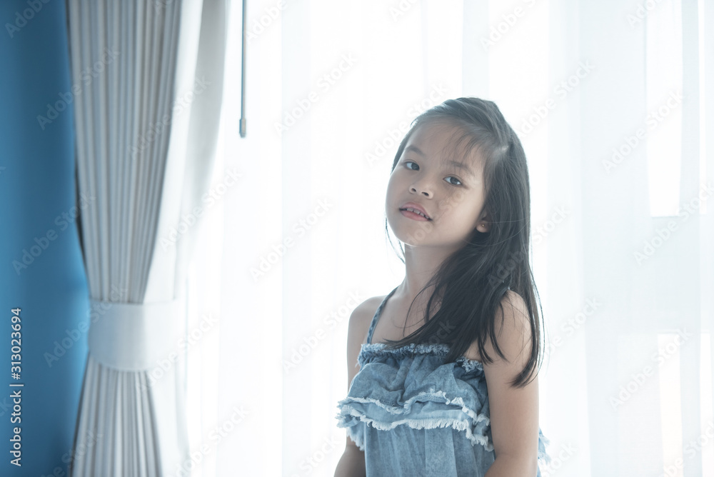A bright, cute girl stood beside the bed in her bedroom. Beautiful little girl smiling. Portrait of cheerful kid lies at windowsill. A bright, cute girl stood beside the bed in her bedroom. Beautiful little girl smiling. Portrait of cheerful kid lies at windowsill.