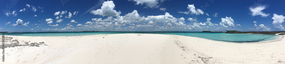Panoramic image of white sand and turquoise waters underneath a bright blue sky with white puffy clouds in the Sea of Abaco in the Bahamas