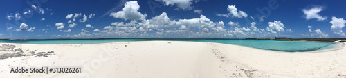 Panoramic image of white sand and turquoise waters underneath a bright blue sky with white puffy clouds in the Sea of Abaco in the Bahamas