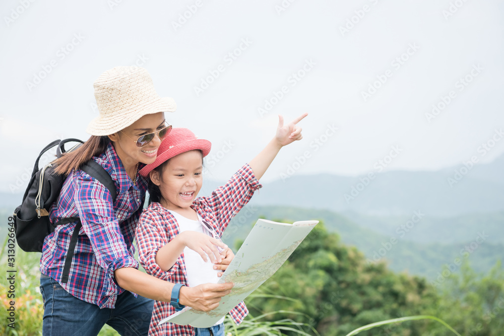 Fototapeta premium Mother and daughter stand on the mountain, pointing their hands forward. With a backpack and wearing a hat, standing, checking the map, with mountains in the background. Travel and adventure concepts
