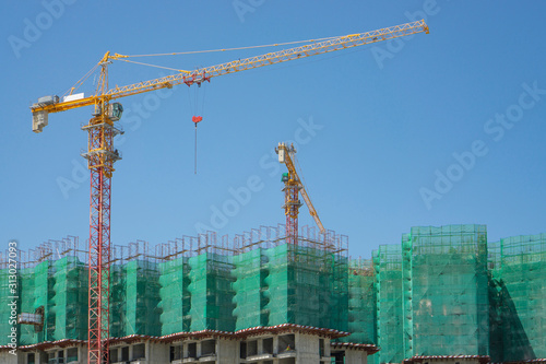 Upward view of precast building cover by green net, large tall Tower Crane moving machine in construction work, under clear blue sky photo