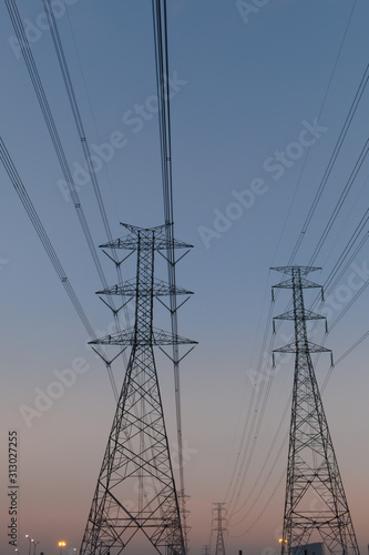 A picture of a high-voltage electricity pole made of steel, with many wires passing across in the evening sky background.