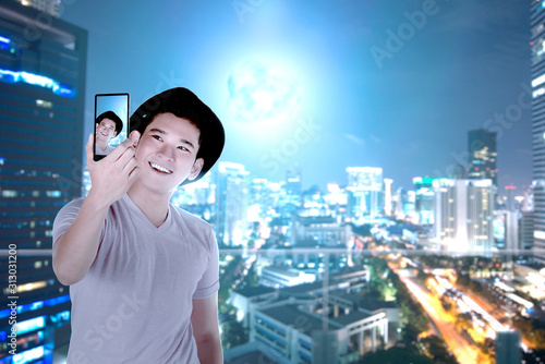 Asian man in hat making selfie using the camera phone with skyscrapers background