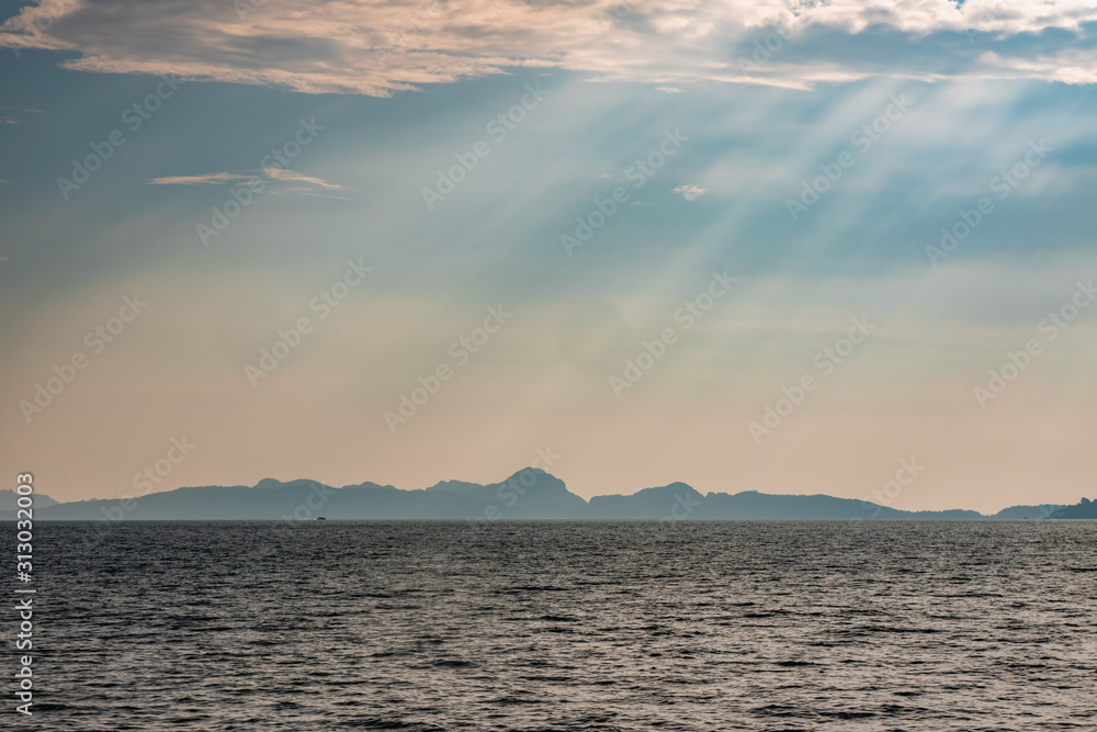 Dramatic sun rays hitting the sea off the coast of Thailand. Hills of Phi Phi Island can be seen in the background. Dramatic sun rays hitting the sea off the coast of Thailand. Hills of Phi Phi Island can be seen in the background.