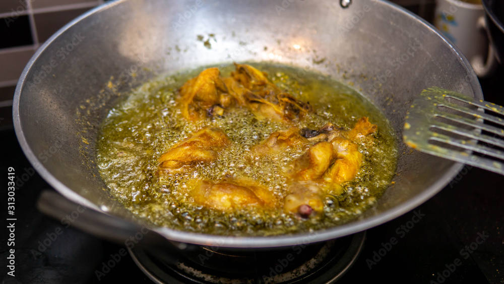 Close up view of a raw chicken meat fried in a wok with hot boiling oil at the kitchen. Close up view of a raw chicken meat fried in a wok with hot boiling oil at the kitchen.