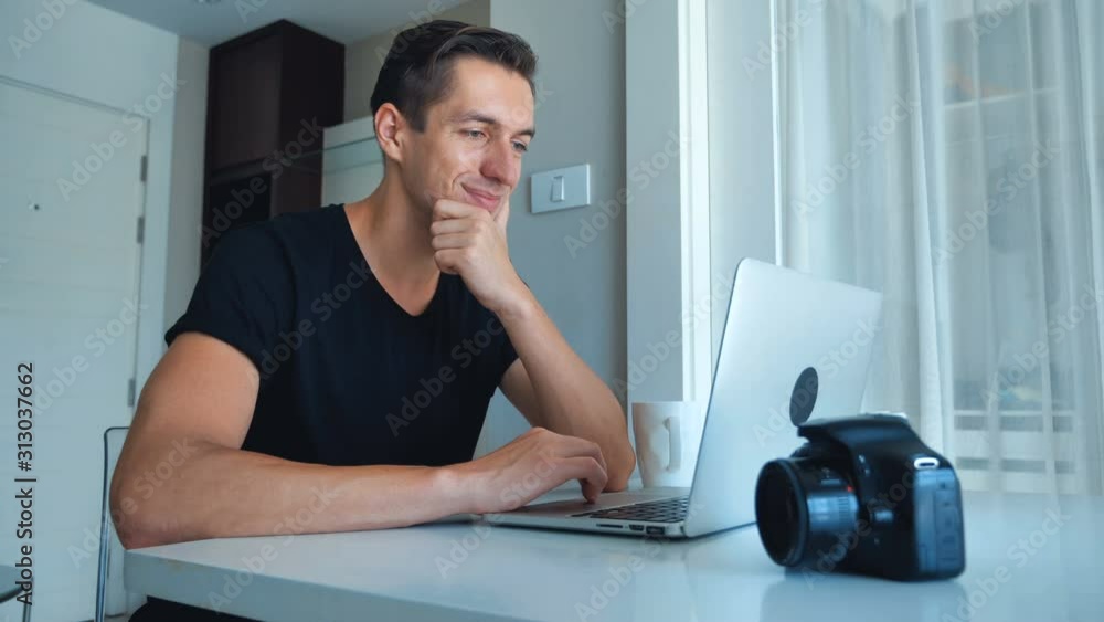 Young photographer using laptop processing images on his laptop at home. Camera, External Hard Drive Lie Beside. Young photographer using laptop processing images on his laptop at home. Camera, External Hard Drive Lie Beside.