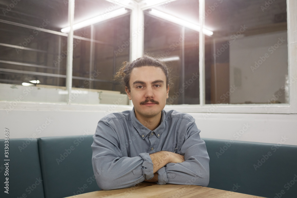 Portrait of young man with moustache sitting at the table and looking at camera at office Portrait of young man with moustache sitting at the table and looking at camera at office