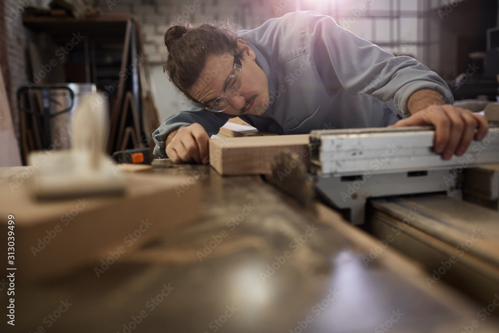 Carpenter in protective eyeglasses measuring the wooden plank using special equipment for measurement he working in the plant Carpenter in protective eyeglasses measuring the wooden plank using special equipment for measurement he working in the plant