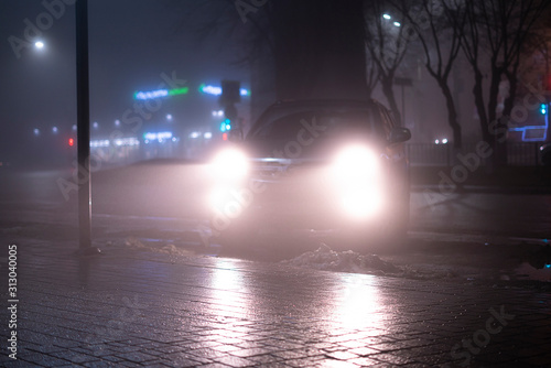 the car headlights through the fog, poor and dangerous driving conditions, night time in the city