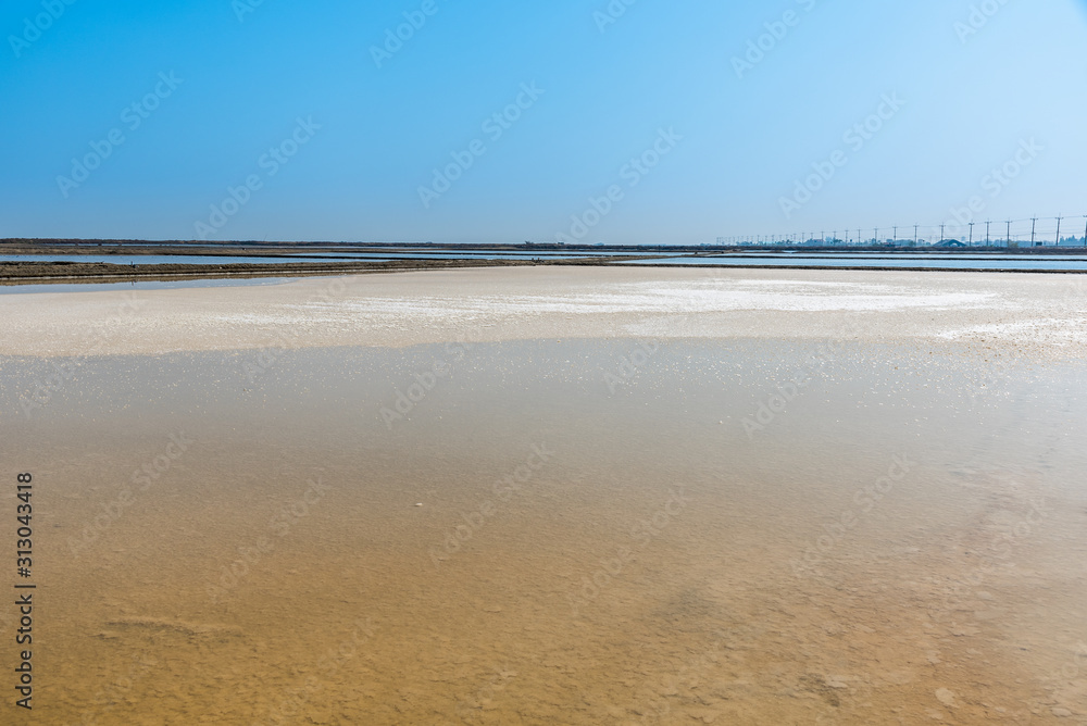 Background of sea water prepare in the salt field to let it dry from sun with blue sky in Thailand, The crystallization of seawater turns into small white pellets