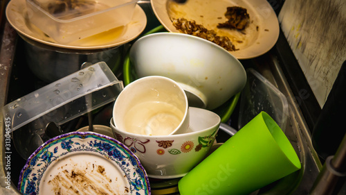 Dirty dishes, utensil, plastic container and food waste piled in a metal sink at the kitchen.