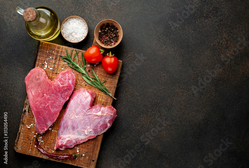 two raw beef steaks in the shape of a heart with spices for cooking dinner for Valentine's day on a stone background with copy space for your text