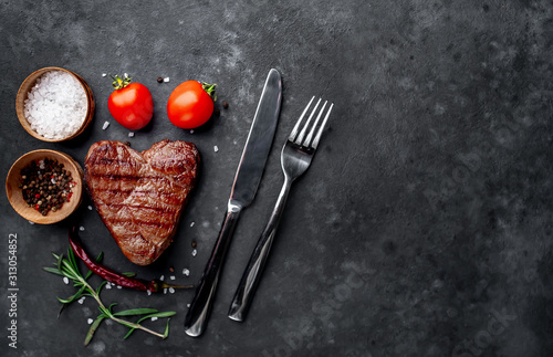 grilled beef steak in the form of a heart with spices, a knife and a fork for Valentine's Day on a stone background with copy space for your text