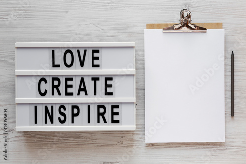Fototapeta Naklejka Na Ścianę i Meble -  'Love create inspire' words on a lightbox, clipboard with blank sheet of paper on a white wooden surface, top view. Overhead, from above, flat lay.