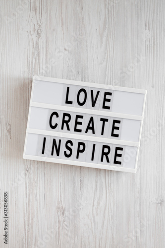 'Love create inspire' words on a modern board on a white wooden background, top view. Overhead, from above, flat lay.