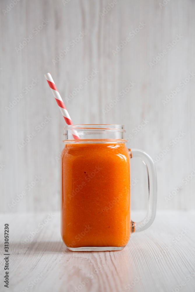 Homemade Mango Carrot Smoothie in a glass jar mug over white wooden background, side view. Close-up. Homemade Mango Carrot Smoothie in a glass jar mug over white wooden background, side view. Close-up.