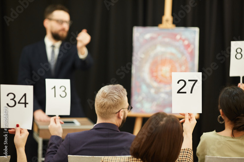 Rear view of group of business people with signs buying a painting during the auction
