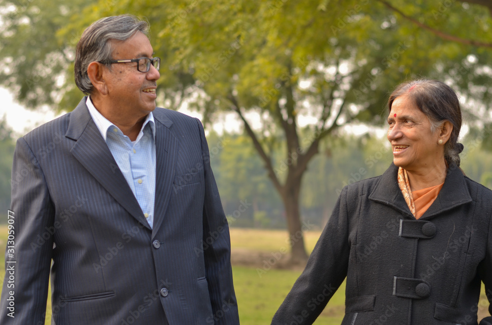 Carefree & happy elder man in black suit, holding his wife hand who is wearing black coat walking in a park in winter in New Delhi, India. Concept love & togetherness Carefree & happy elder man in black suit, holding his wife hand who is wearing black coat walking in a park in winter in New Delhi, India. Concept love & togetherness