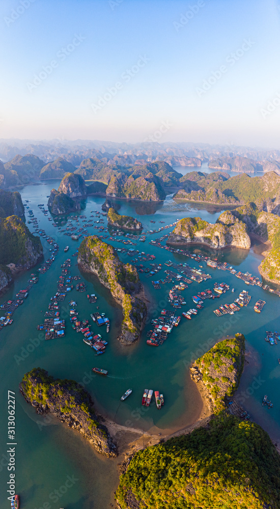 Aerial sunset view of Lan Ha bay and Cat Ba island, Vietnam, unique limestone rock islands and karst formation peaks in the sea, floating fishermen villages and fish farms from above. Clear blue sky.