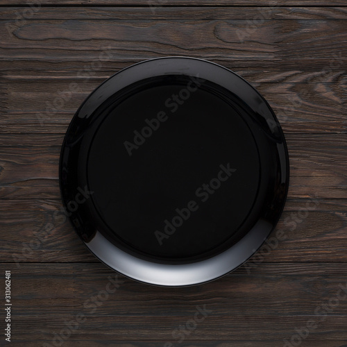 Empty black plate on a wooden table, top view