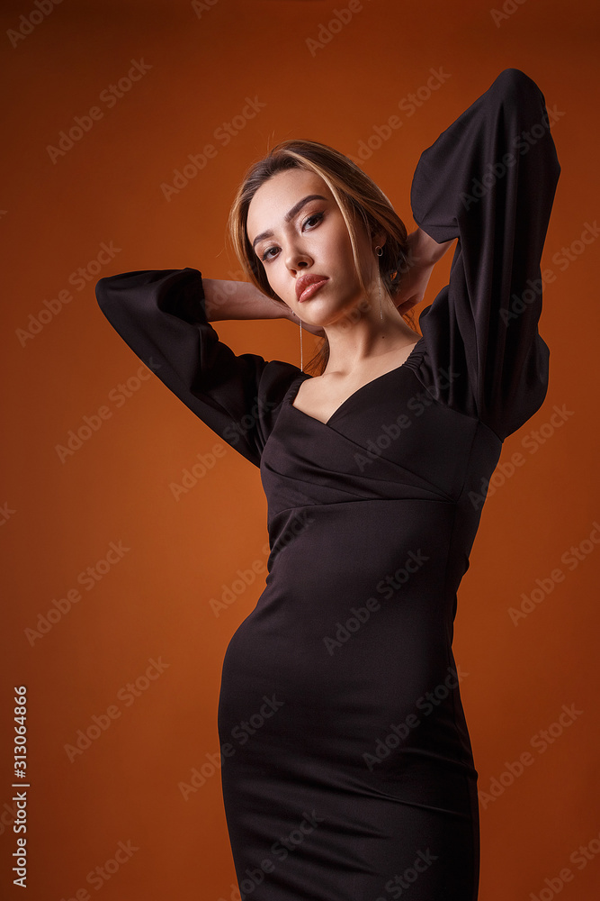 charming elegant fashion model wearing black dress with deep neckline  posing on orange background. asian skinny young woman sits in sexy evening  gown. beautiful sensual glamorous girl poses in studio Photos