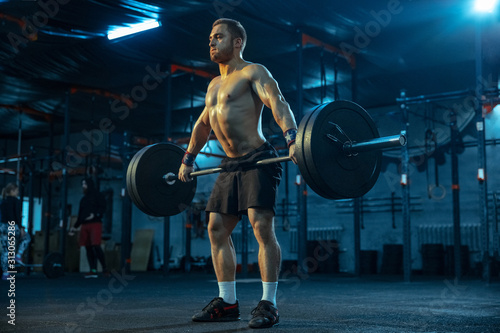 Caucasian man practicing in weightlifting in gym. Caucasian male sportive model training with barbell, looks confident and strong. Body building, healthy lifestyle, movement, activity, action concept.
