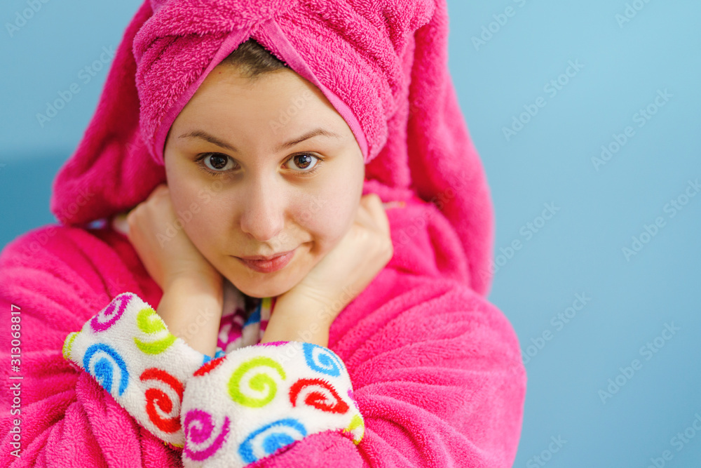 Portrait of young beautiful caucasian woman wearing bathrobe and pink towel on her hair head in front of the blue wall Portrait of young beautiful caucasian woman wearing bathrobe and pink towel on her hair head in front of the blue wall