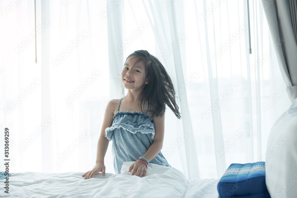 A bright, cute girl stood beside the bed in her bedroom. Beautiful little girl smiling. Portrait of cheerful kid lies at windowsill. A bright, cute girl stood beside the bed in her bedroom. Beautiful little girl smiling. Portrait of cheerful kid lies at windowsill.