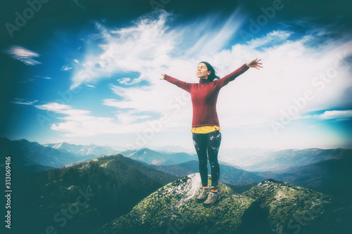 The young girl at the top of the mountain raised her hands up on blue sky background. The woman climbed to the top and enjoyed her success. Dramatic light