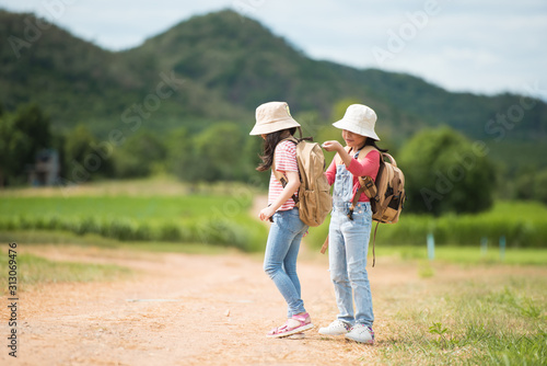 Two children carrying a backpack in the back and wearing a hat for a walk on a country road. She walked and enjoyed the surrounding nature. She enjoys traveling during the summer. © nareekarn