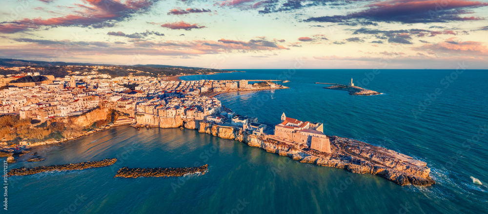 Panoramic view from flying drone. Amazing morning cityscape of Vieste - coastal town in Gargano National Park with Castello Svevo, Italy, Europe. Bright spring sunrise on Adriatic sea.