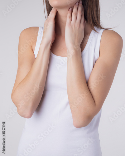 Closeup of sick young woman suffering from throat problems, holding hands on her lymph nodes, isolated. Thyroid gland, painful swallowing concept. Inflammation of the upper respiratory tract