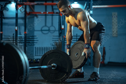 Caucasian man practicing in weightlifting in gym. Caucasian male sportive model preparing for training, looks confident and strong. Body building, healthy lifestyle, movement, activity, action concept