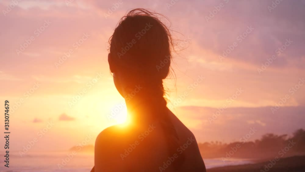 SLOW MOTION Smiling relaxed young woman in bikini with braided hair watching the sunset on a tropical beach over the shoulder SLOW MOTION Smiling relaxed young woman in bikini with braided hair watching the sunset on a tropical beach over the shoulder