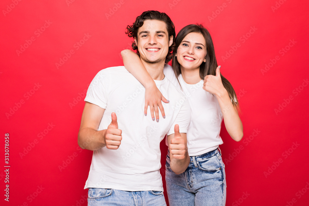 Photo of cheerful couple smiling showing in white t-shirt thumb up with excitement on face isolated a red background Photo of cheerful couple smiling showing in white t-shirt thumb up with excitement on face isolated a red background