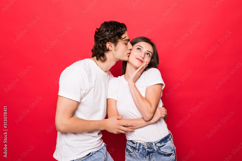 Fototapeta premium Portrait of beautiful smiling couple kissing over red background.